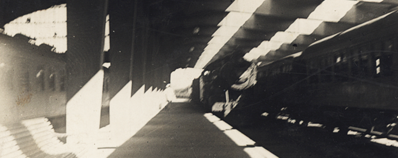 Fotografia de acervo, em preto e branco, mostrando a estação de trem Roosevelt, com bancos, pilastras e dois trens, um chegando e outro parado
