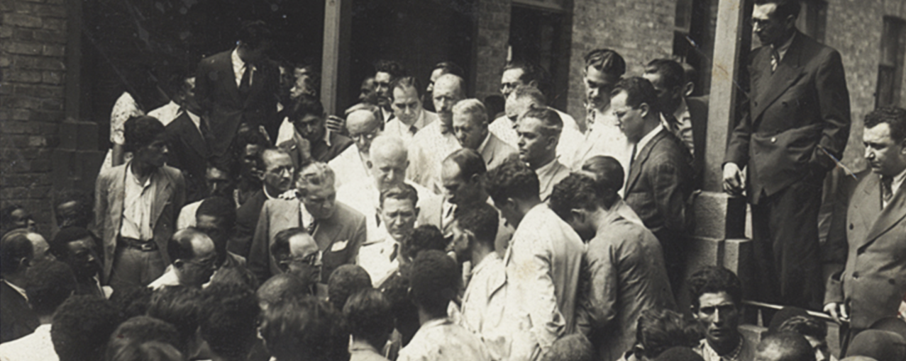 Em preto e branco, mostra um grupo de homens ao redor do então presidente Getúlio Vargas, em um dos espaços da Hospedaria do Brás
